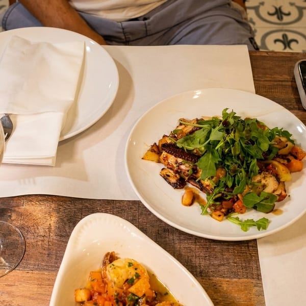 A table set with white wine, red wine, and plates of octopus salad and shrimp.